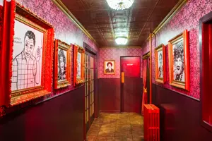 Hallway with funky wallpaper and portraits of famous queer people throughout history, including James Baldwin